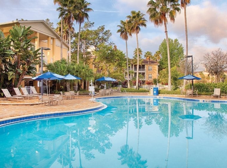Outdoor resort pool surrounded by pool chairs and palm trees at Club Wyndham Cypress Palms, a timeshare resort in Kissimmee, FL.