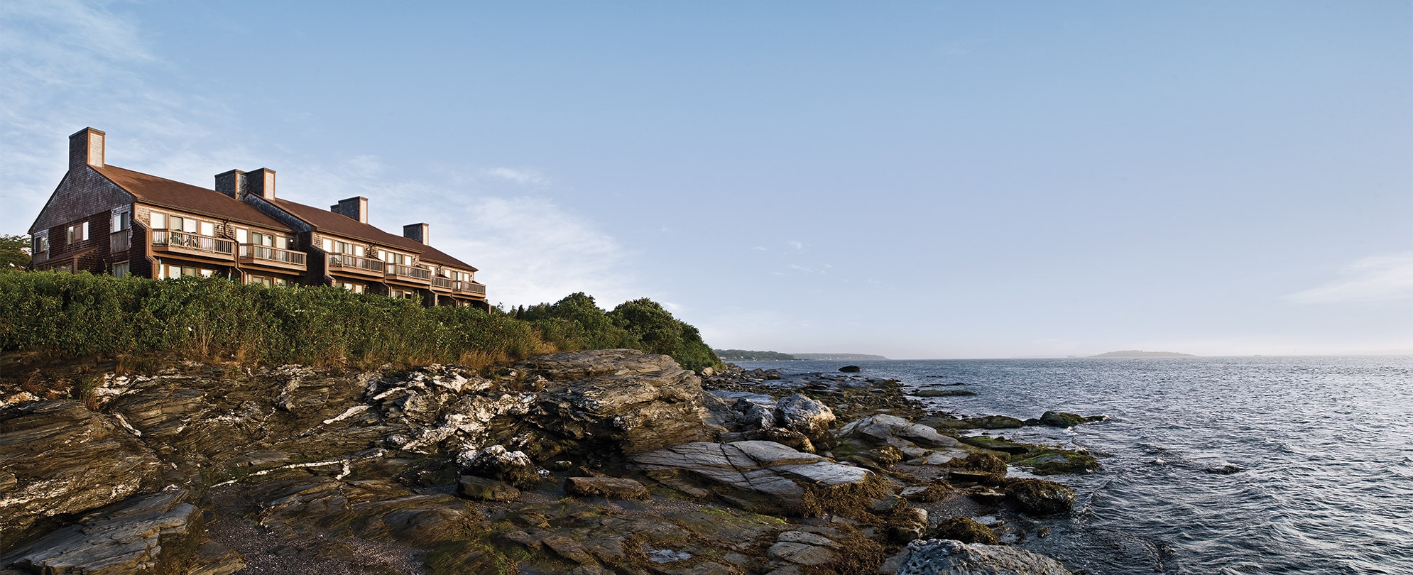 The exterior of Club Wyndham Newport Overlook, a timeshare resort in Newport, RI on a rocky shoreline.