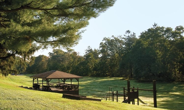  Grass-covered hills and pine trees surrounding wooden picnic tables, a gazebo, and a playground on the property of Club Wyndham Shawnee Village resort.