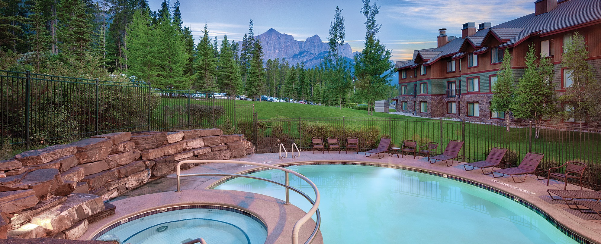 The outdoor pool and hot tub at WorldMark Canmore Banff, a timeshare resort, with the Canadian Rocky Mountains in the distance.
