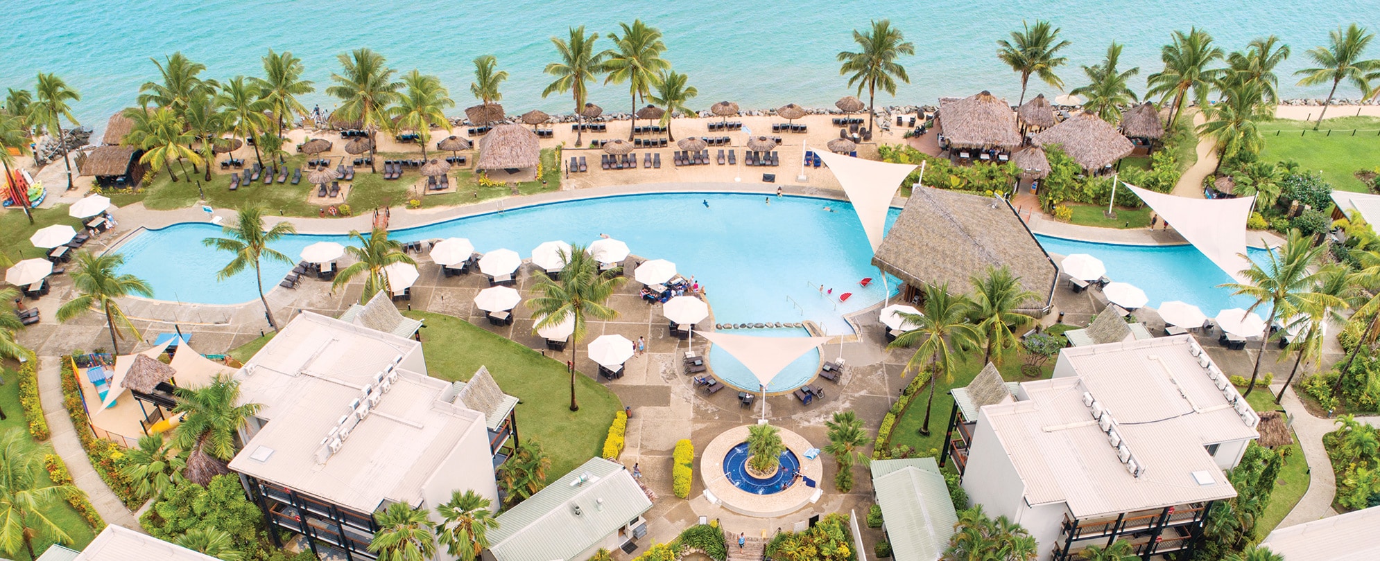 An aerial view of the pool with palm trees and pool umbrellas overlooking the ocean at Club Wyndham Denarau Island.