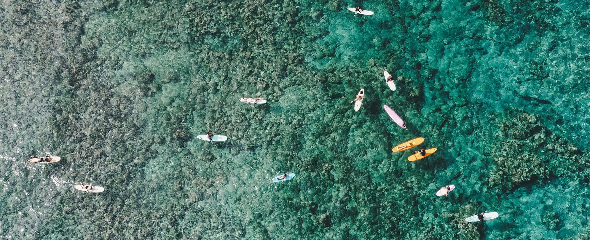 Aerial image of surfers sitting on their surfboards in the emerald-green waters surrounding Kona, Hawaii.