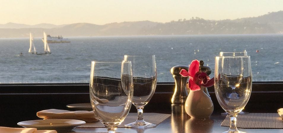 View from inside a waterfront restaurant of set table with four glasses overlooking the San Francisco Bay..